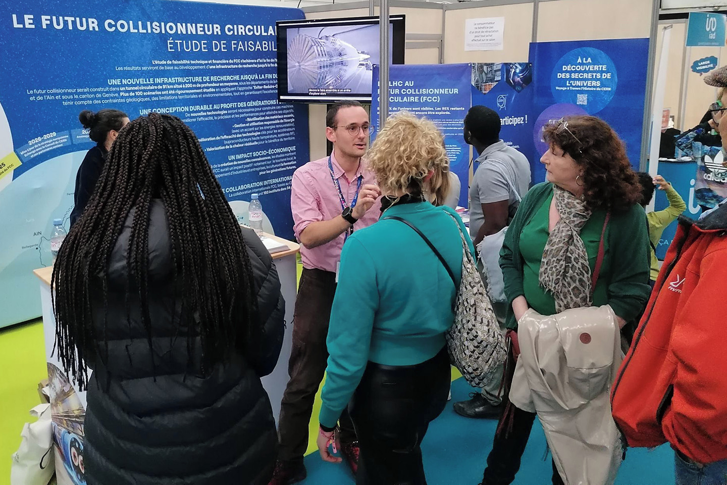 A white male speaking to visitors surrounded by information boards at the event