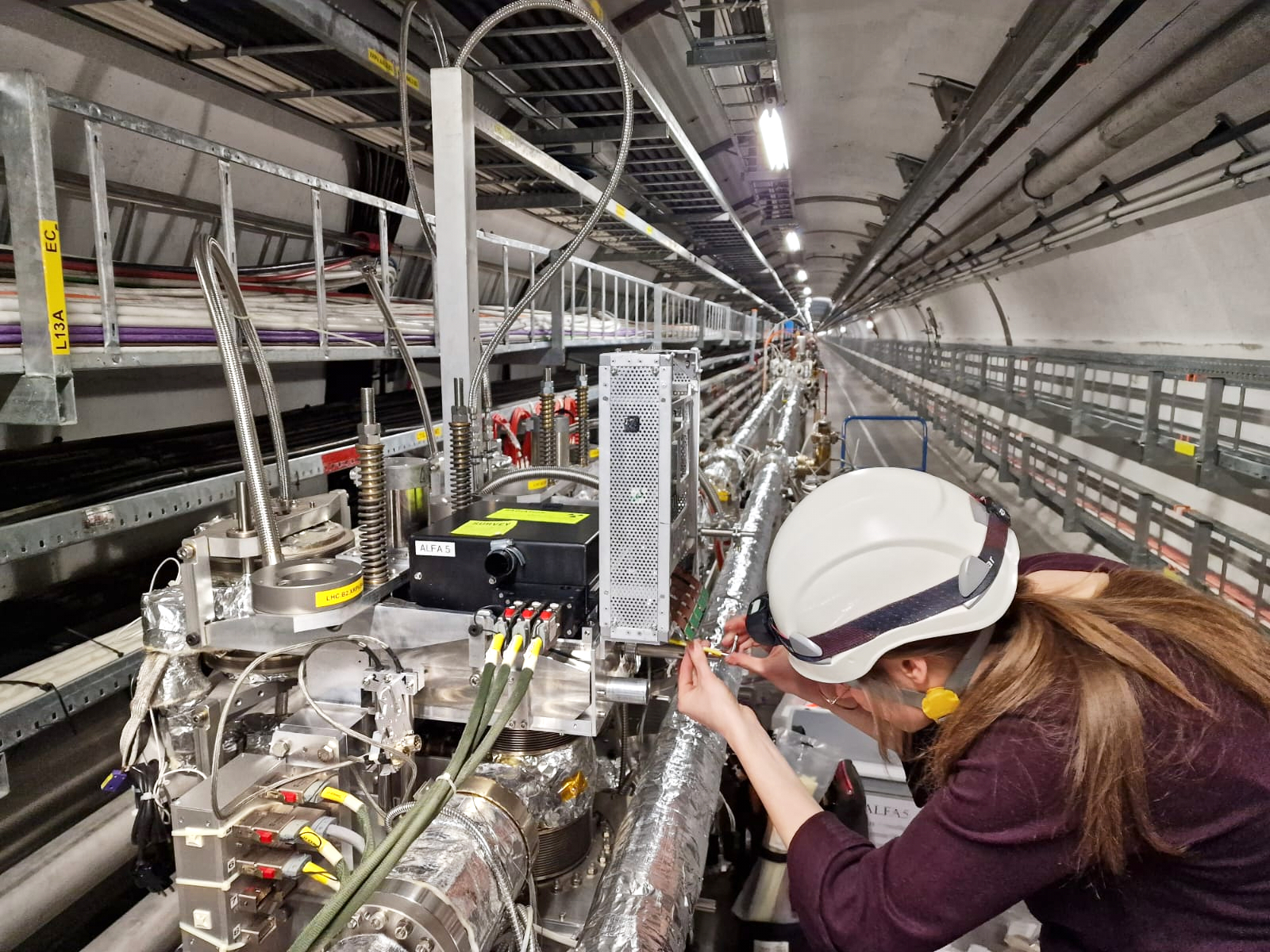 A woman bending down to screw on some equipment in the LHC tunnel.