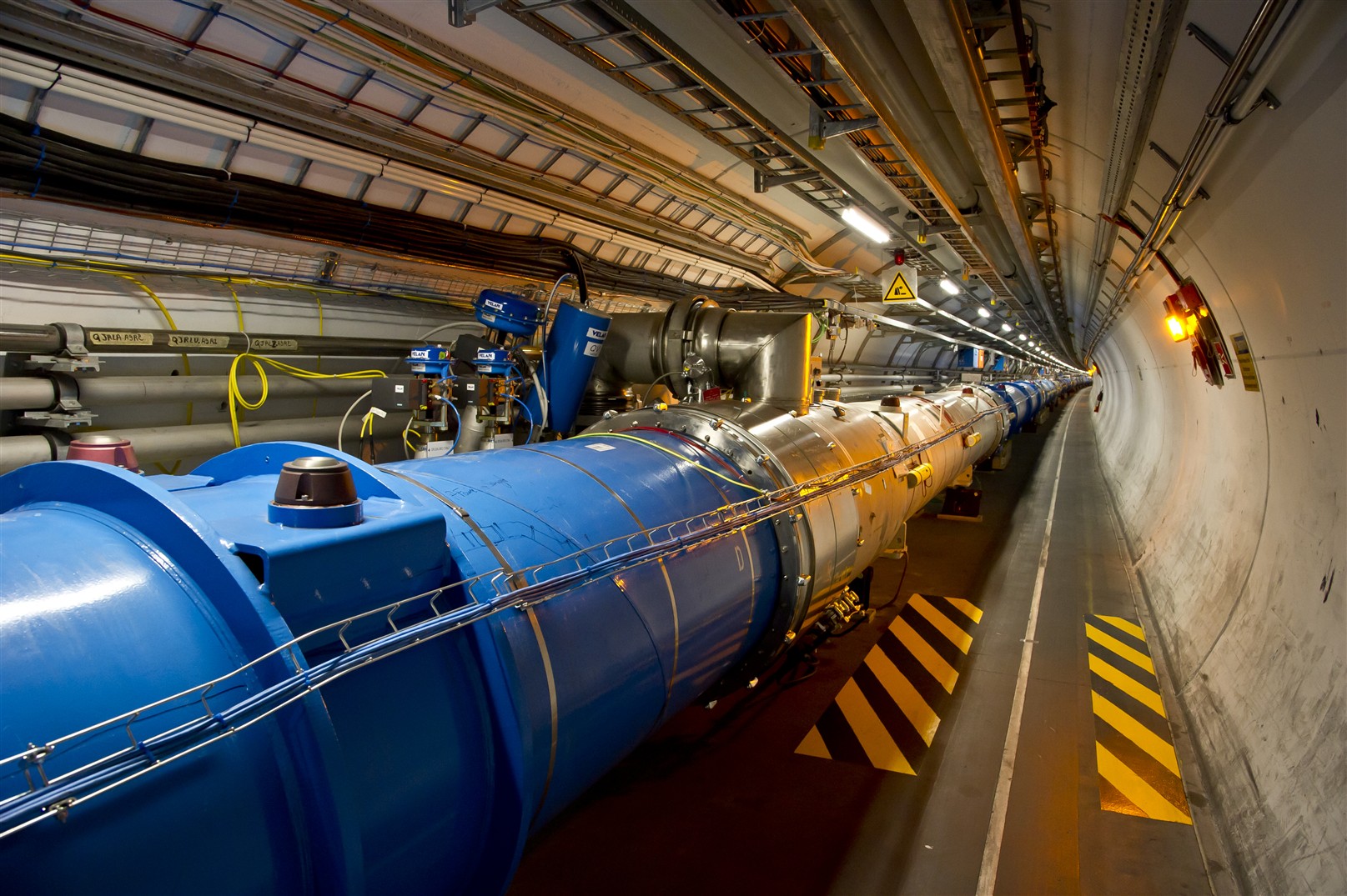 A very long cylindrical tunnel with a large blue and silver metal tube, the LHC, running down the length of it. There are lots of cables and neatly organised around the LHC.