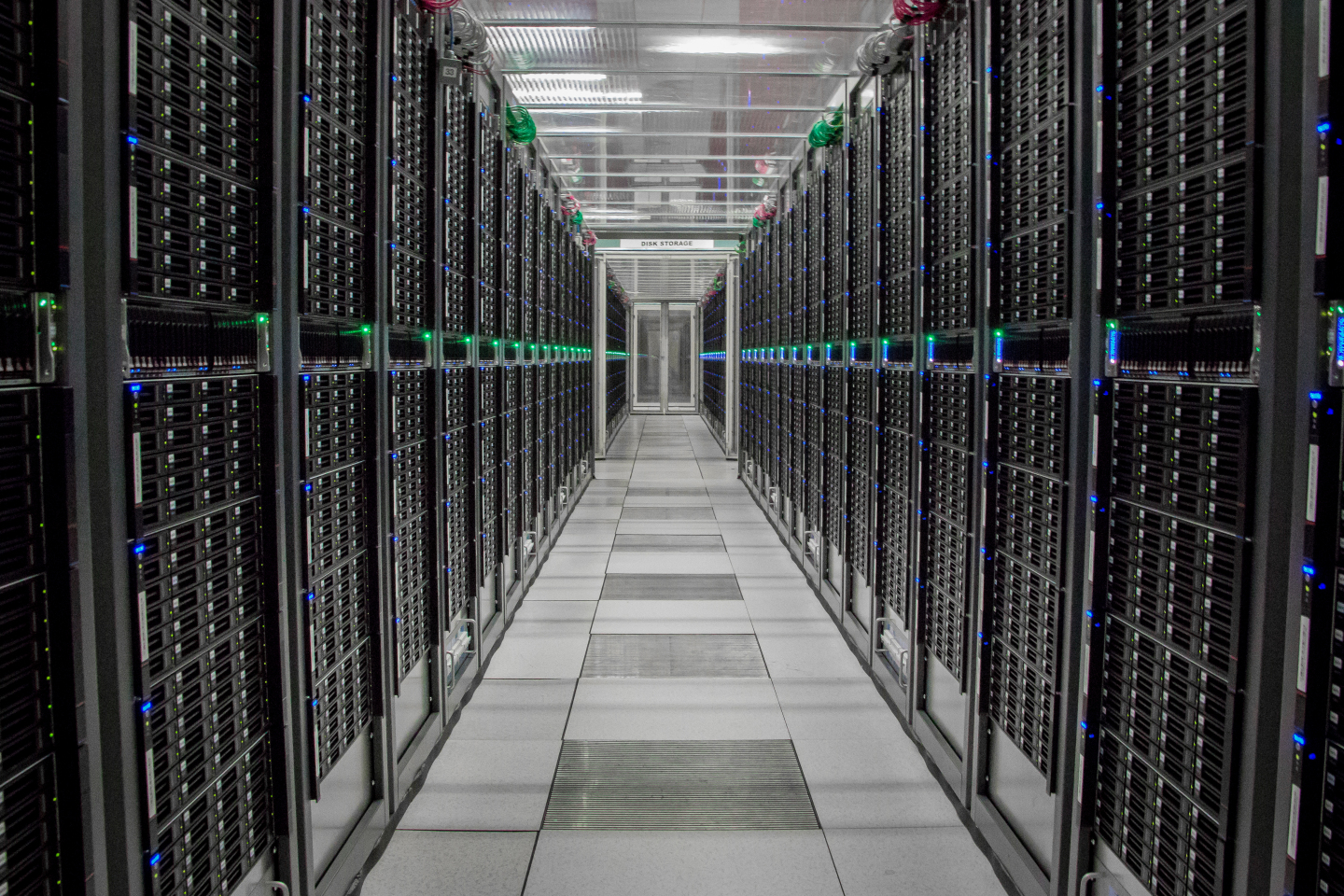 a corridor between two walls of black computing elements with green and blue tiny lights