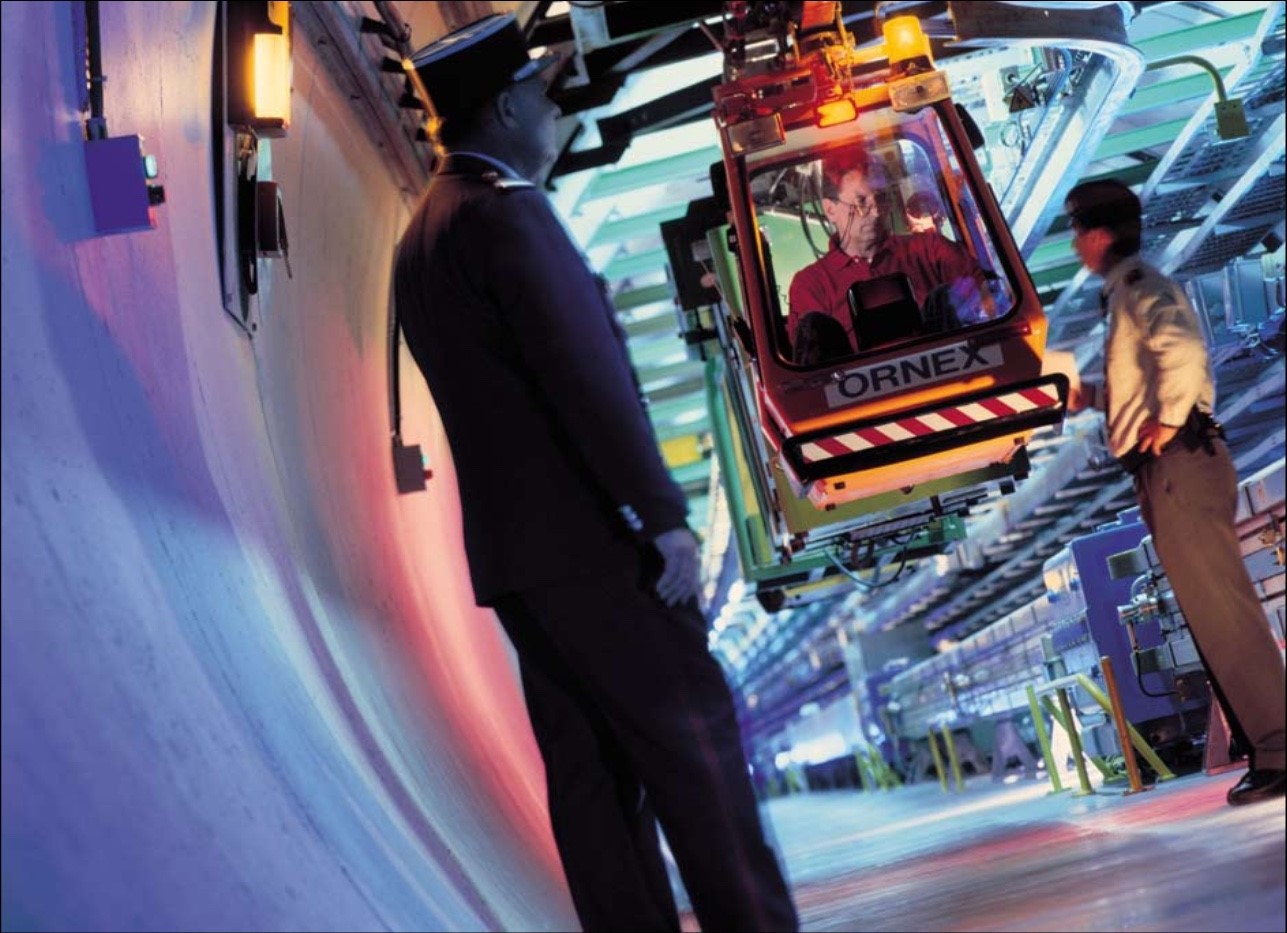 Two border guards underground with a person travelling on a monorail suspended from the ceiling